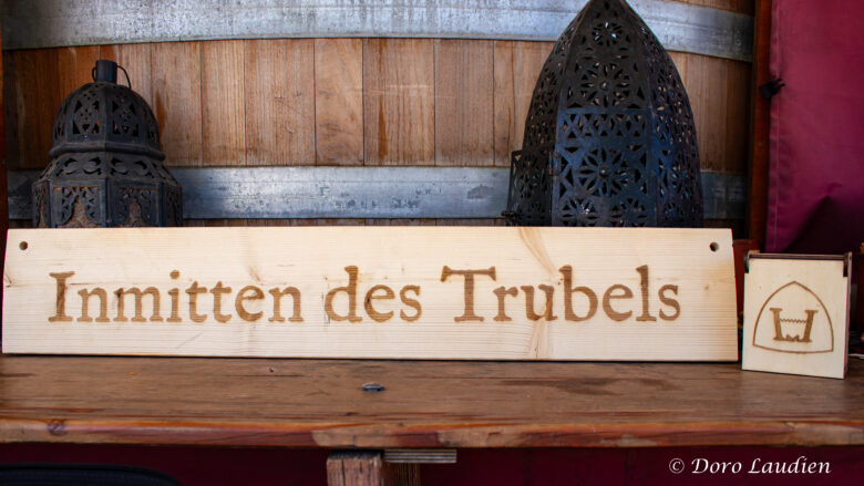 Ein etwa ein Meter langes Holzschild, darauf ist in großen Lettern graviert "Inmitten des Trubels".