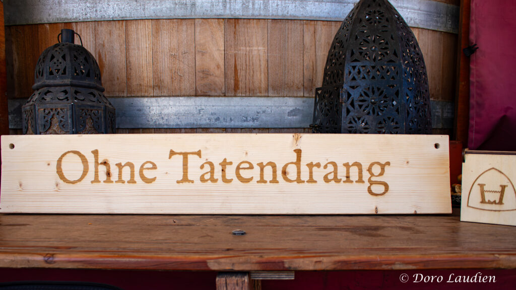 Ein etwa ein Meter langes Holzschild, darauf ist in großen Lettern graviert "Ohne Tatendrang".